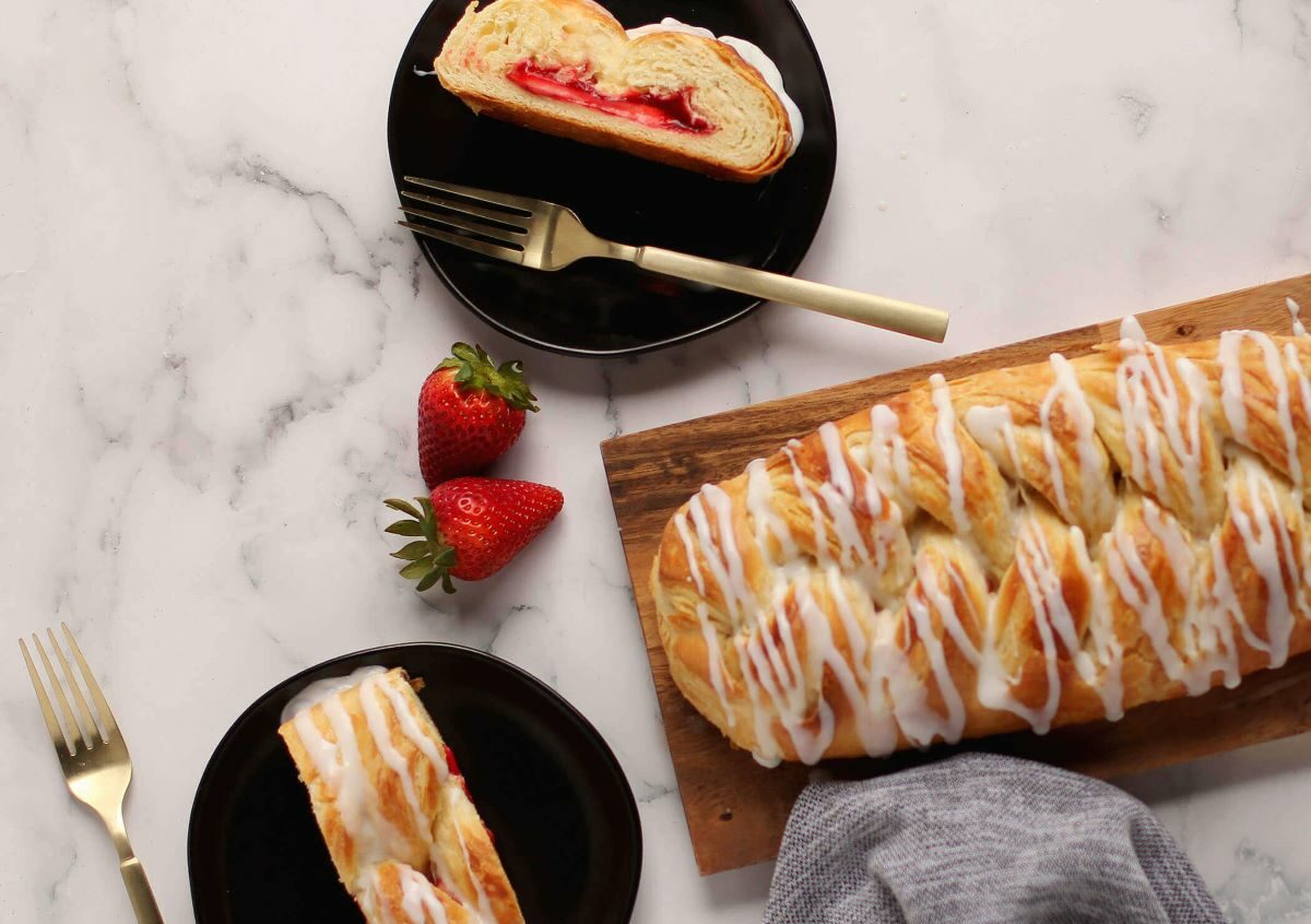 Strawberry Cream Cheese Butter Braid Pastry next to two plates with slices of pastry, forks, and strawberries